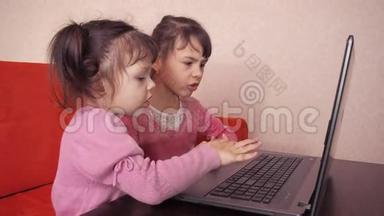 孩子们在笔记本电脑里玩。 两个<strong>小</strong>女孩印在笔记本电脑上。 两个<strong>姐姐</strong>坐在橙色<strong>的</strong>沙发上看着一圈